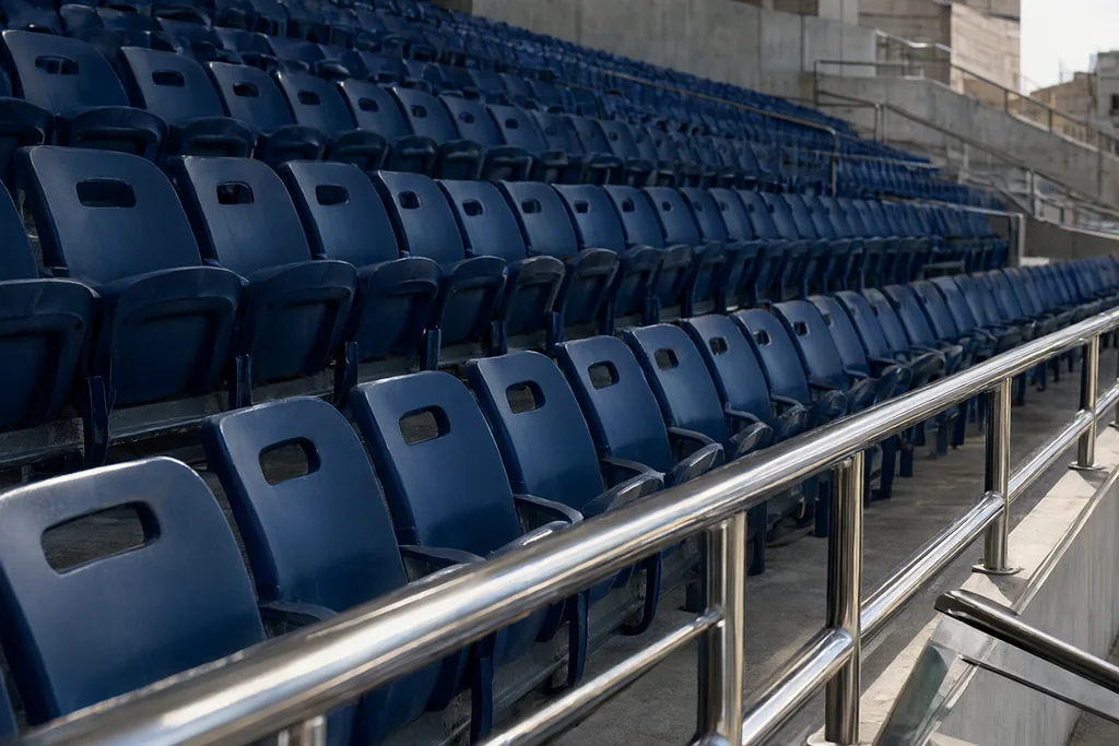 Row of empty stadium seats beside a steel handrail in daylight